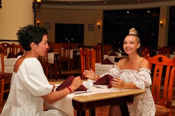 Two lonely cheerful women are sitting in an empty hotel restaurant