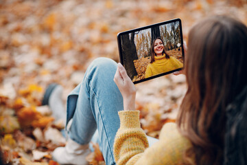 Young woman model take selfie photo with tablet pc in autumn park with yellow foliage maple leaves. Fall season fashion
