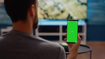 Person holding mobile phone with green screen vertically on display sitting in living room at home....
