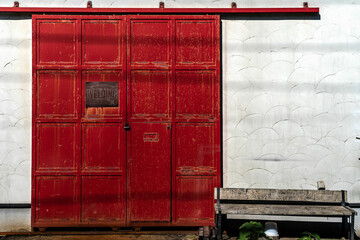 A large door with white wall and old wood bench. No people is there.