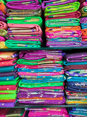 Artistic variety shade tone colors ornaments patterns, closeup view of stacked saris or sarees in display of retail shop.