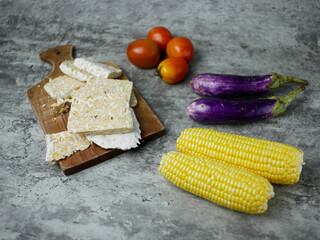 the concept of healthy food on the kitchen table consists of eggplant, tomatoes, corn and tempeh. vegetarian food