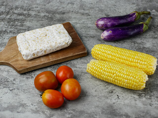 the concept of healthy food on the kitchen table consists of eggplant, tomatoes, corn and tempeh. vegetarian food