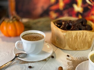 On the wooden table by the fireplace are white cups with coffee and gingerbread cookies in a wooden bowl