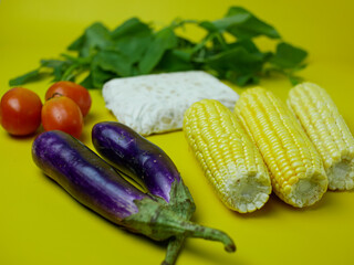 the concept of healthy food consists of eggplant, spinach, tomatoes, and corn. vegetarian food. isolated on a yellow background