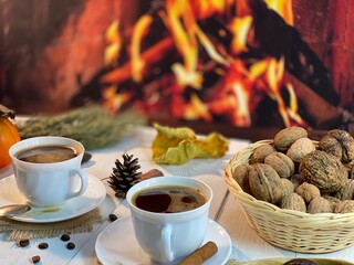 On the wooden table by the fireplace are white cups with coffee and a basket of nuts
