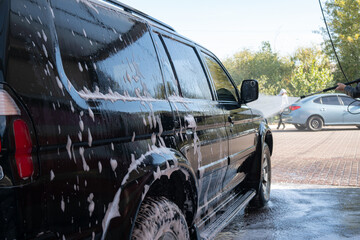 self-service car wash, black jeep is washed with foam and water
