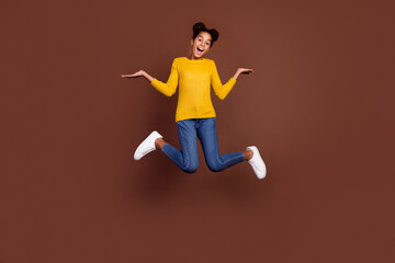 Fototapeta na wymiar Full body photo of small girl jump hold empty space wear shirt jeans shoes isolated on brown color background