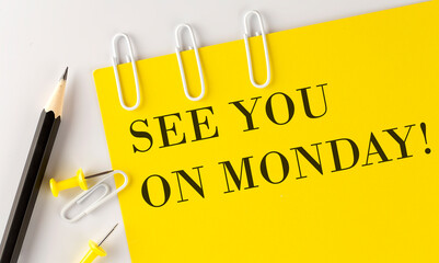 SEE YOU ON MONDAY word on the yellow paper with office tools on the white background