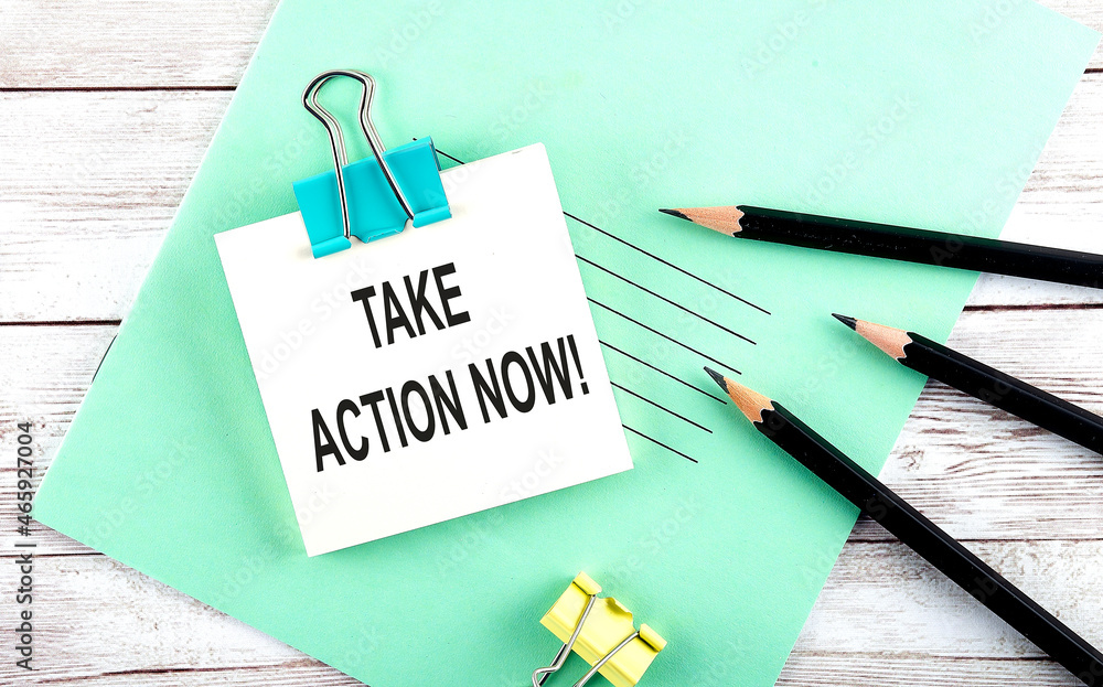 Poster stickers with pencils and notebook with text take action now on wooden background