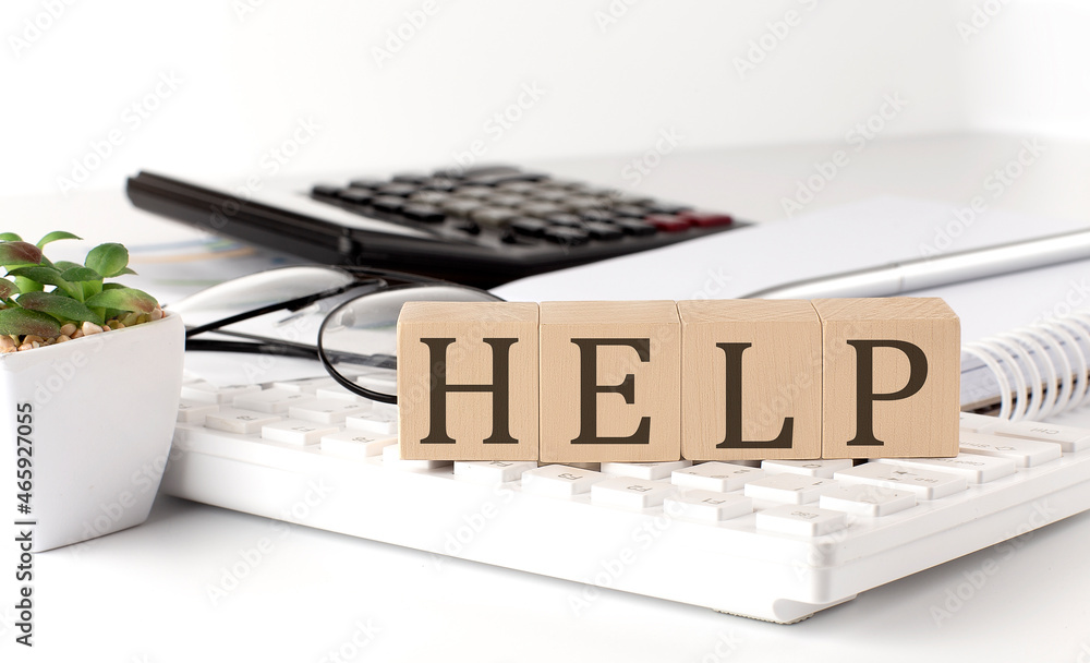 Aufkleber help written on a wooden cube on keyboard with office tools