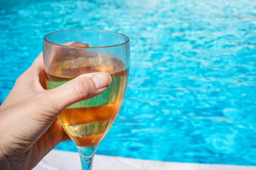 female hand toasting with the white wine at swimming pool