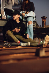A teenage skater is sitting with his friends outdoors and drinking beer. © chika_milan