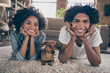 Photo of happy positive dark skin young couple lie carpet dog lover enjoy weekend indoors inside...