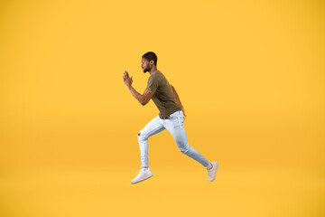 Fototapeta na wymiar Young african american man running over yellow studio background, in motion side view shot of guy jumping in air