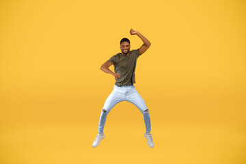 Fototapeta na wymiar Expressing joy. Full length studio shot of active black man jumping over yellow background, free space