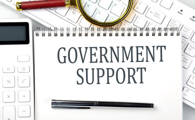 GOVERNMENT SUPPORT Text on the notepad with calculator and keyboard