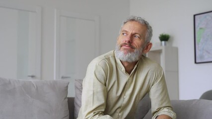 Dreamy relaxed mature older thoughtful tattooed hipster man relaxing sitting and thinking at home. Pensive calm stylish mid aged single bearded guy resting on couch at home looking away, reflecting.