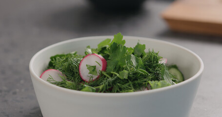 salting fresh salad with radish, cucumber and herbs in white bowl