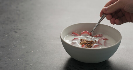 man hand eat chocolate granola with strawberries and yogurt on a concrete countertop