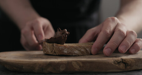 man spreading chocolate hazelnut spread on ciabatta slice on wood board