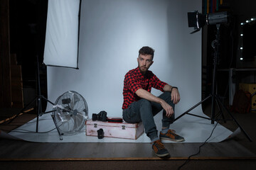 young stylish photographer in studio surrounded by lighting equipment