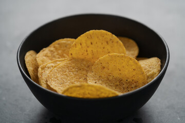 Round nachos in black ceramic bowl on concrete background
