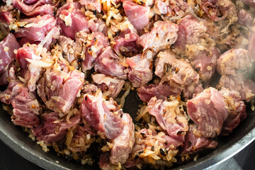 above view of pieces of raw beef frying with finely chopped onions closeup in deep frying pan at home kitchen