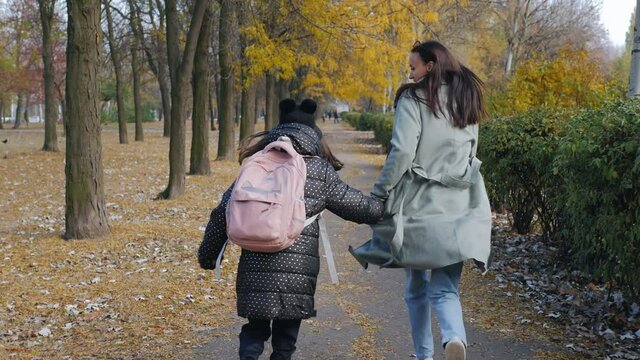 Mom and little daughter are running through the autumn park to school. Be late for school.
