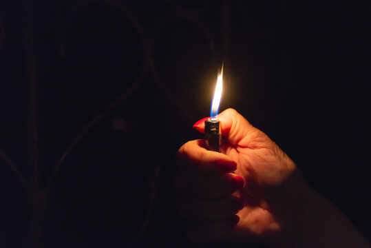 Woman hand holding a burning lighter in the dark black background.Closeup,selective focus.Copy space.