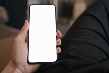 Man hold smartphone with white screen in his hand sitting on a couch in home environment