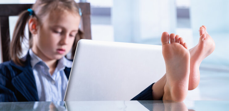 Humorous photo of happy child business girl is resting and working at the same time. Selective focus on bare feet. Horizontal image.