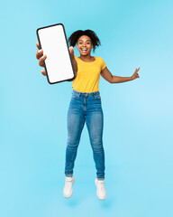 Great new mobile app. Excited African American woman jumping and showing smartphone with blank...