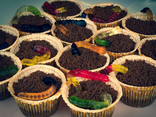 Halloween cupcakes with colorful jelly worms coming out of crumbs as if it is soil. Creative...