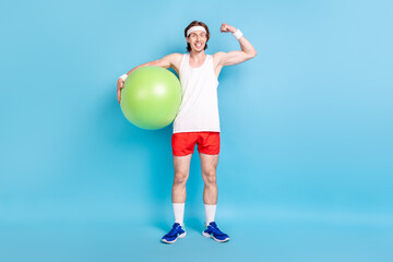 Full length body size photo strong man keeping fit ball showing biceps isolated pastel blue color background