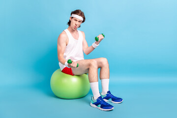 Full length body size photo guy drinking water sitting on rubber fit ball lifting dumbells isolated...