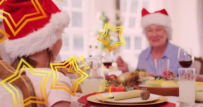 Animation of stars falling over happy caucasian family wearing santa hats and having dinner