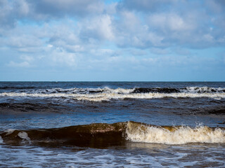Wave with white foamy coastline beach. Sandy shore.