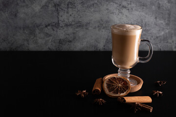 spice coffee with milk and foam, cinnamon sticks on blach background. christmas drink, chai latte