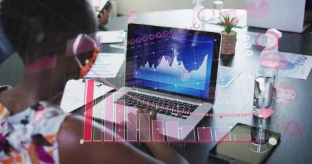 Animation of financial data processing over businesswoman with face mask using laptop in office - Powered by Adobe