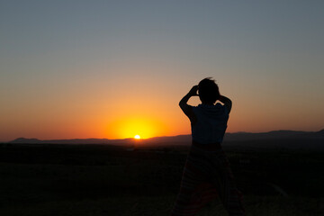 Fototapeta premium Silueta de mujer con los brazos levantados al caer la tarde, puesta de sol