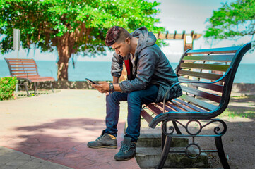 Obraz premium man sitting on a bench checking his phone, young man checking his cell phone sitting on a bench