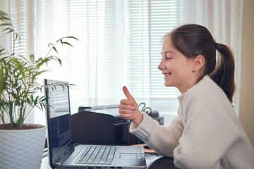 Smiling young girl using computer at home office workplace exploring online communication with pc.