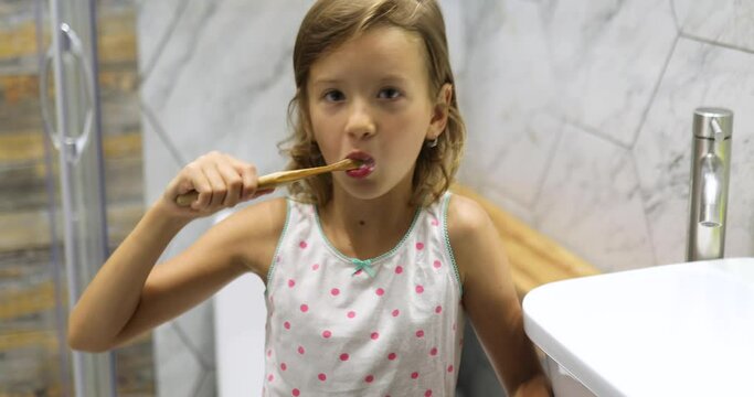 Little Girl brushing teeth with ecologe wooden Toothbrush in the bathroom at home, healthy hygiene concept