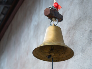 Old brass bell hangs on a cement wall.