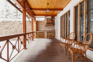 Two wicker chairs stand on veranda on winter day