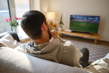 Man on the couch is watching TV. football fan watches football and rejoices at the victory. Entertainment and sports concept. Watching sports, movies on TV at home