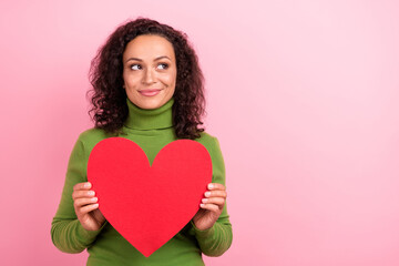 Photo of charming dreamy african lady dressed green turtleneck holding large paper heart looking empty space isolated pink color background