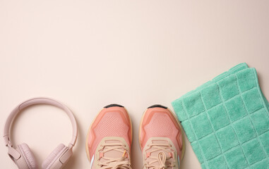 pair of pink textile sneakers, wireless headphones and a textile green towel on a beige background. Set for sports, running
