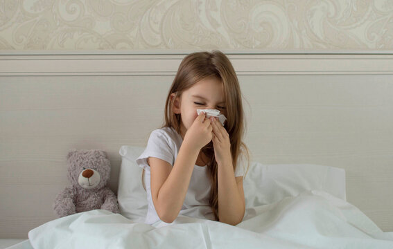 Sick child is sick at home, lying in bed with a teddy bear and blowing his nose in a handkerchief. The sad look of the girl. flu, acute respiratory viral infections, colds. Selective focus.